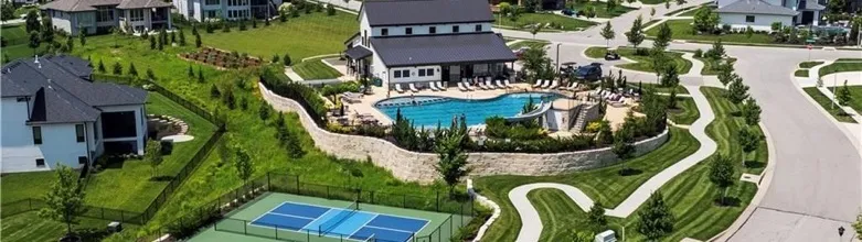 An aerial view of the Century Farms neighborhood pool, clubhouse and pickleball courts with a winding walking trail through green lawns, in Overland Park, Kansas, on a clear summer day