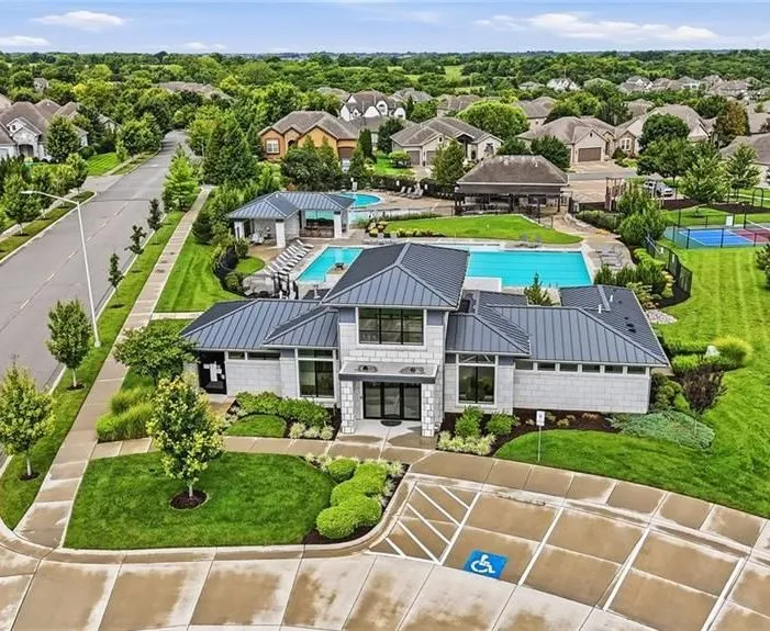 An oblique aerial view of the Chapel Hill neighborhood in Overland Park, Kansas: the clubhouse and pools in the foreground, with pickleball courts, a curving street and homes stretching to the horizon, on a summer day with a cloud-streaked sky