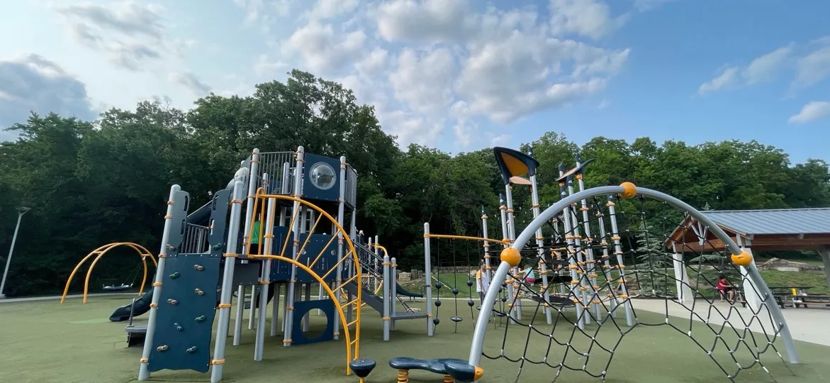 Roe Park, Overland Park, Kansas: a playground with climbing structures and a rope net arch, under a partly cloudy sky