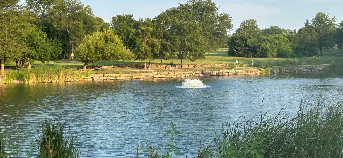 Thomas S. Stoll Memorial Park, Overland Park, Kansas: a pond with a fountain, reeds in front and mature trees along the far bank