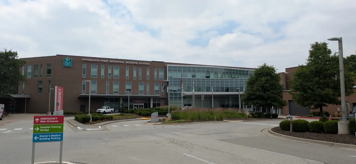 Overland Park Regional Medical Center, Overland Park, Kansas: the brick and glass hospital building across the entrance drive, under a cloudy sky