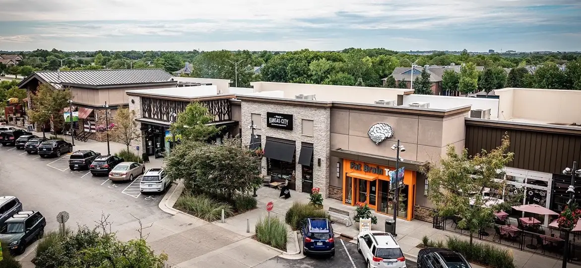 An elevated view of the Prairiefire retail district in Overland Park, Kansas, with shops, patio dining, parking and treetops stretching to the horizon